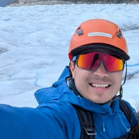 Charlie Lehman, smiling, in a climbing helmet on a glacier